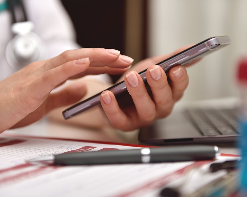 写真、パソコンのあるデスクにて、スマホで電話をかける